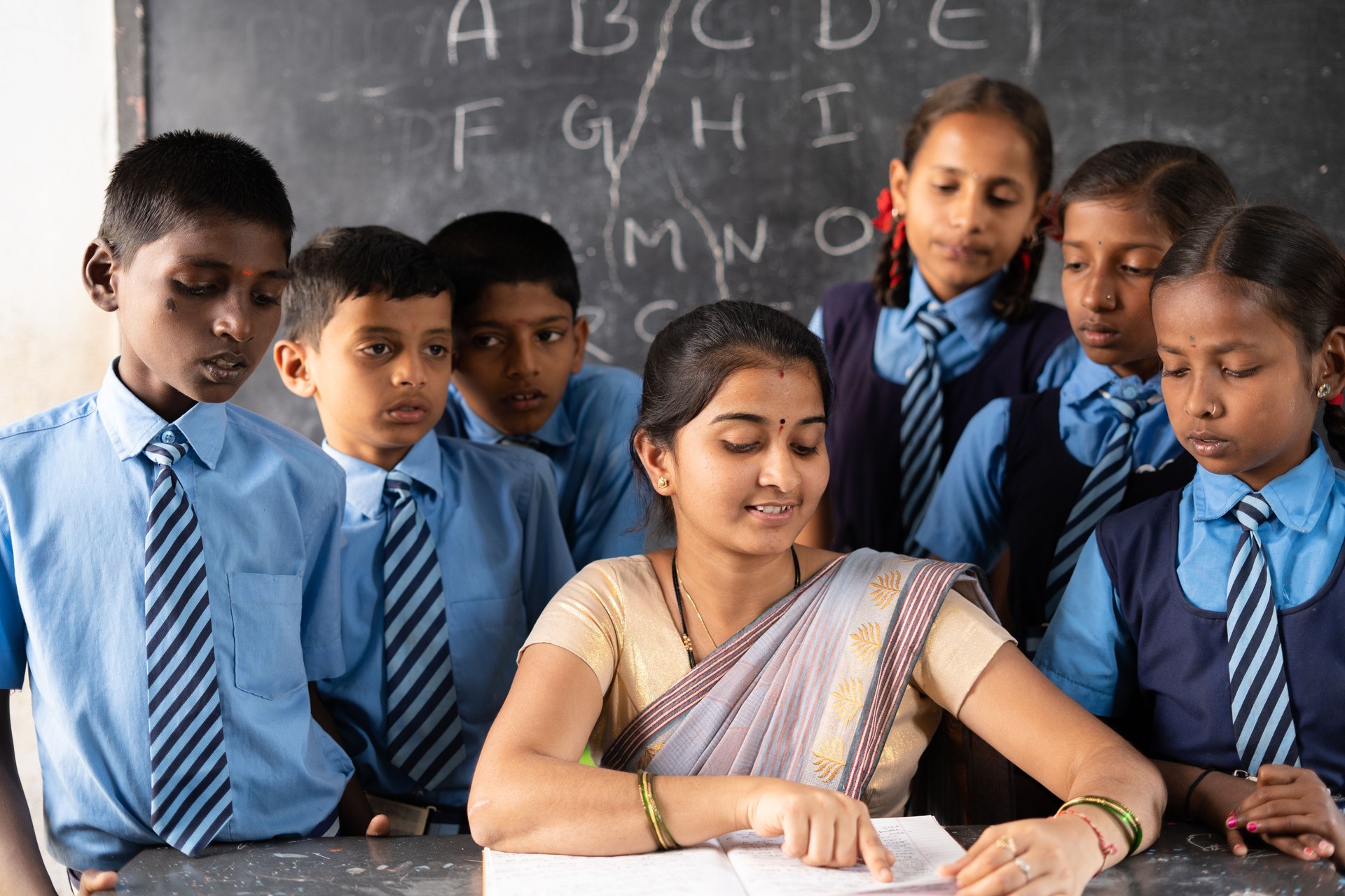 Teacher with students around explaining or teaching from book on classroom - concept of support, education, assistance and guidance
