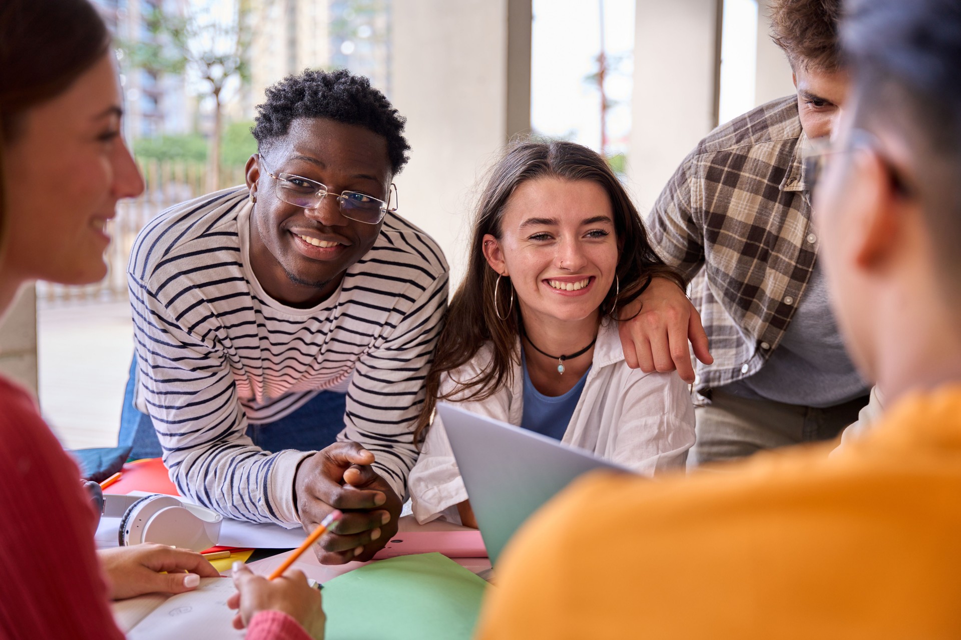 Cheerful multiracial couple of young students working together with classmates sitting in faculty.